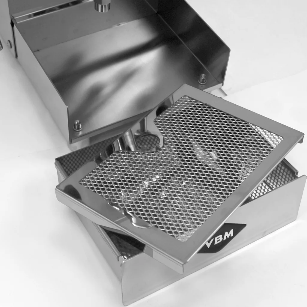A stainless steel drip tray with a removable grid, partially open to reveal its interior, branded with the VBM logo and made for the DISCONTINUED - VBM Domobar Junior HX Espresso Machine. © 2025 1st-line.com