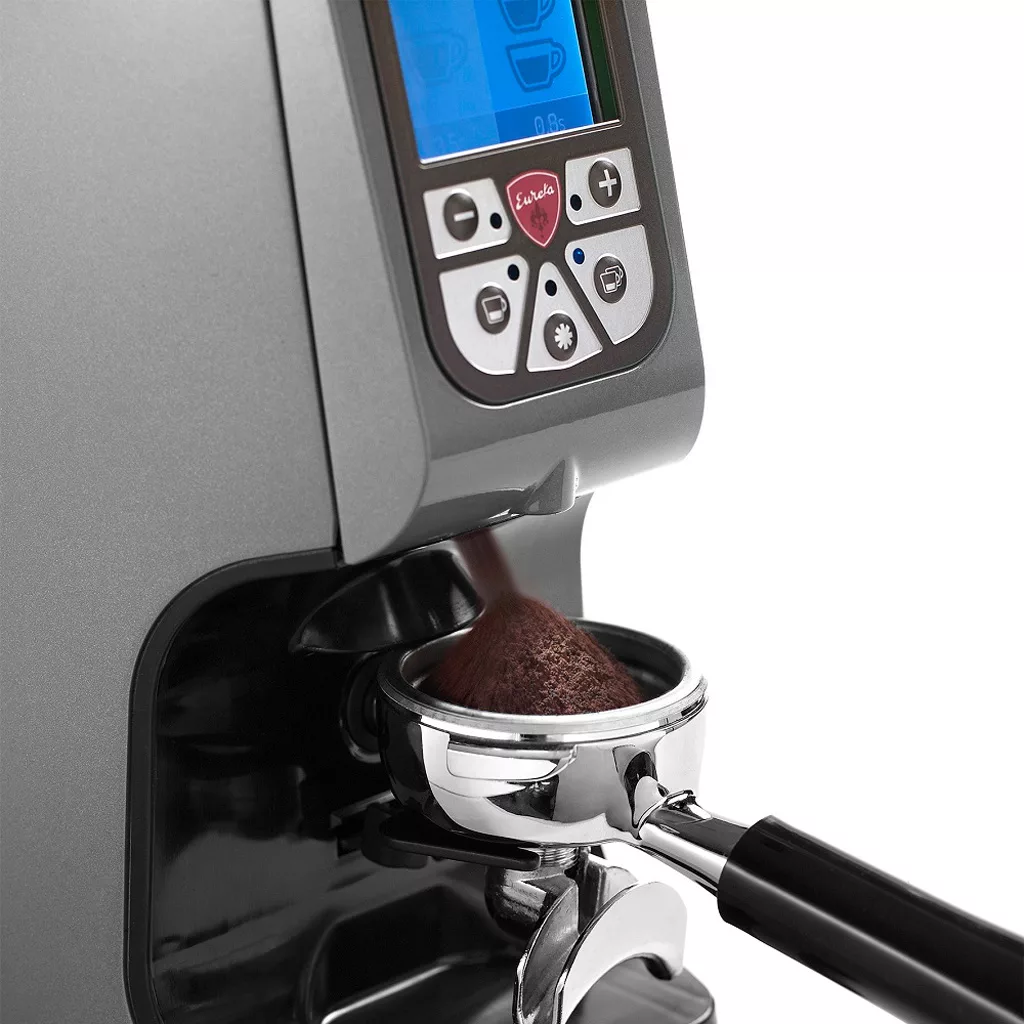Close-up of an espresso machine dispensing fresh ground coffee into a portafilter, with the Eureka Atom 60 Espresso Coffee Grinder and its digital control panel visible above. © 2025 1st-line.com