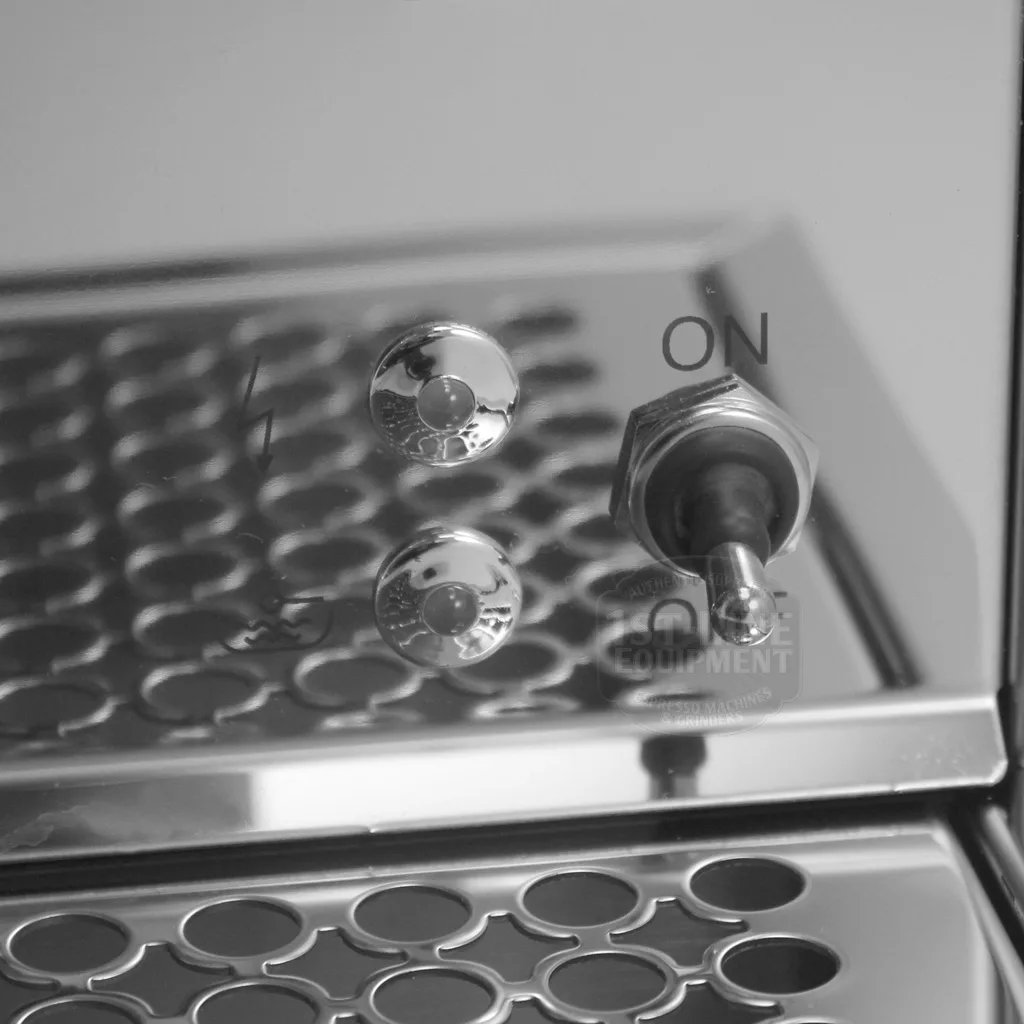 A close-up of a metallic switch panel from the DISCONTINUED Bezzera BZ07 PM Espresso Machine, featuring a toggle switch in the ON position and two round buttons, reflected on a shiny perforated metal surface. © 2025 1st-line.com