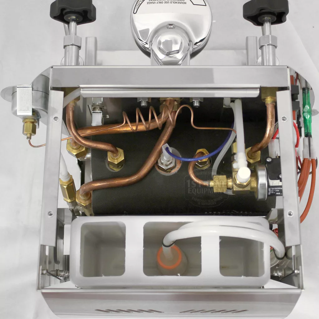 Top-down view of the DISCONTINUED La Nuova Era Cuadra HX Espresso Machine with its top cover removed, displaying internal components such as copper pipes, a black cylindrical boiler, wiring, and a white plastic water reservoir. © 2025 1st-line.com
