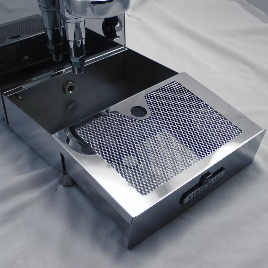 A close-up of the shiny, stainless steel drip tray with a perforated grate from the DISCONTINUED VBM Domobar Super V4 Dual Boiler PID Switchable Espresso Machine, shown on a white surface. © 2025 1st-line.com