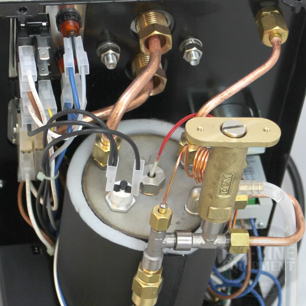 Close-up of the discontinued ECM Classika PID Espresso Machines internals, showing copper pipes, a metal boiler, wires, and brass fittings in a compact assembly—highlighting this product’s quality craftsmanship. © 2025 1st-line.com
