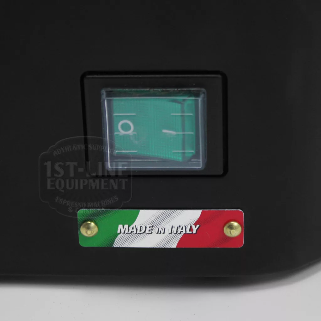 A close-up of the DISCONTINUED Quamar M80 Semi-Automatic Doser Espresso Coffee Grinder gauge with a green face in a black panel. Below is a label featuring Italian flag colors, MADE IN ITALY in white, secured by two gold screws. © 2025 1st-line.com
