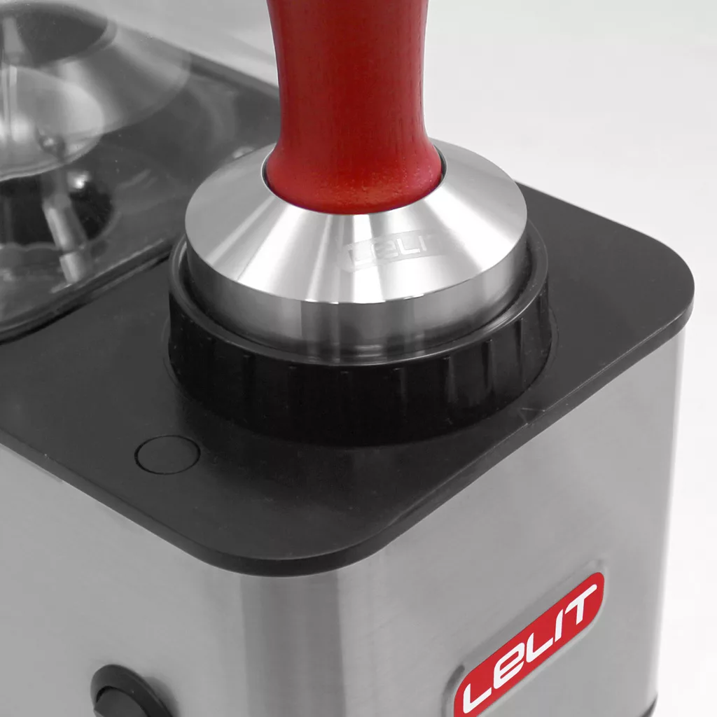 A close-up of a stainless steel Lelit espresso machine with a metal and red-handled tamper on a black rubber tamping station, next to the DISCONTINUED Lelit PL71 William Espresso Coffee Grinder. © 2025 1st-line.com