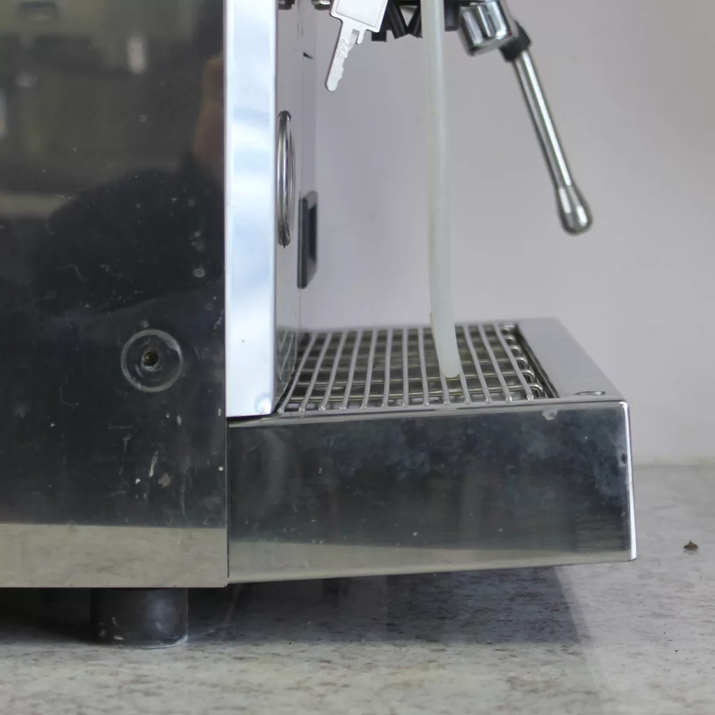 A close-up side view of the (SOLD) SIDEWALK SALE - ECM Veronica Espresso Machine USED E002 E502 shows its steam wand and flexible drain tube above a metal drip tray, positioned on a countertop. © 2025 1st-line.com
