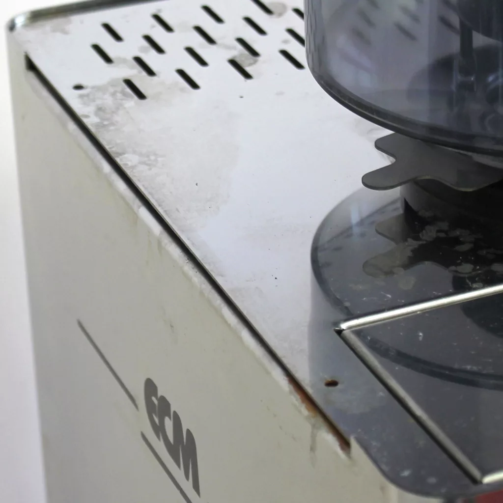 Close-up of the ECM Veronica Espresso Machine (SOLD) SIDEWALK SALE - USED E002 E502, showing water stains, light rust on stainless steel, part of the grinding chamber, and the ECM logo. © 2025 1st-line.com