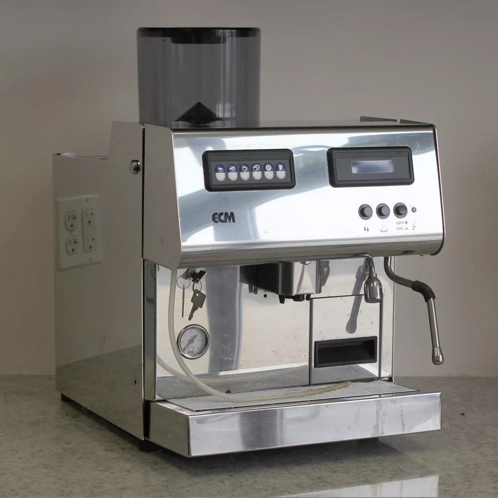 The (SOLD) SIDEWALK SALE - ECM Veronica Espresso Machine USED E002 E502, with digital controls and a sleek stainless steel design, sits elegantly on a countertop against a plain wall. © 2025 1st-line.com