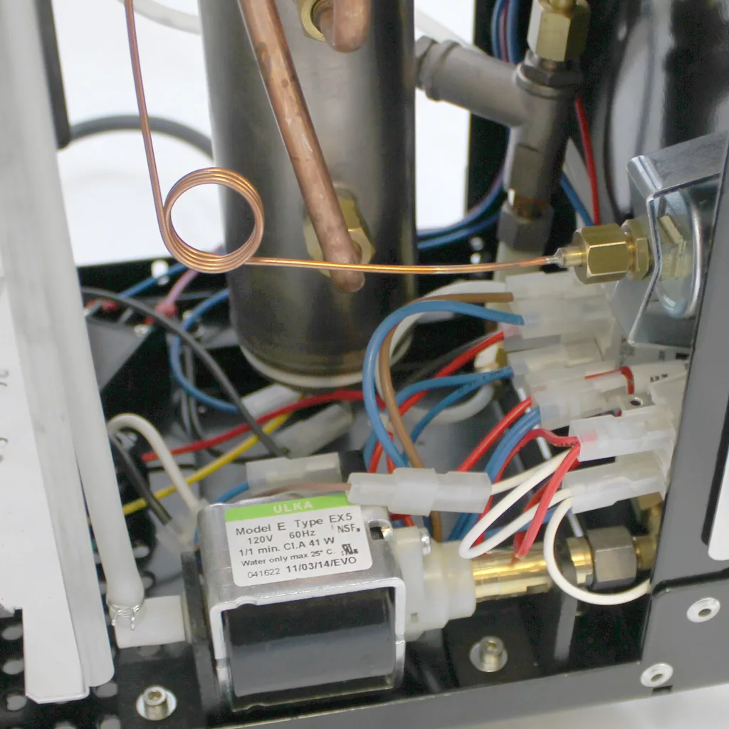 Close-up of electrical components and wiring inside the Bezzera Unica Espresso Machine, showing a solenoid valve, copper tubing, wires, and connectors mounted on a metal frame. © 2025 1st-line.com