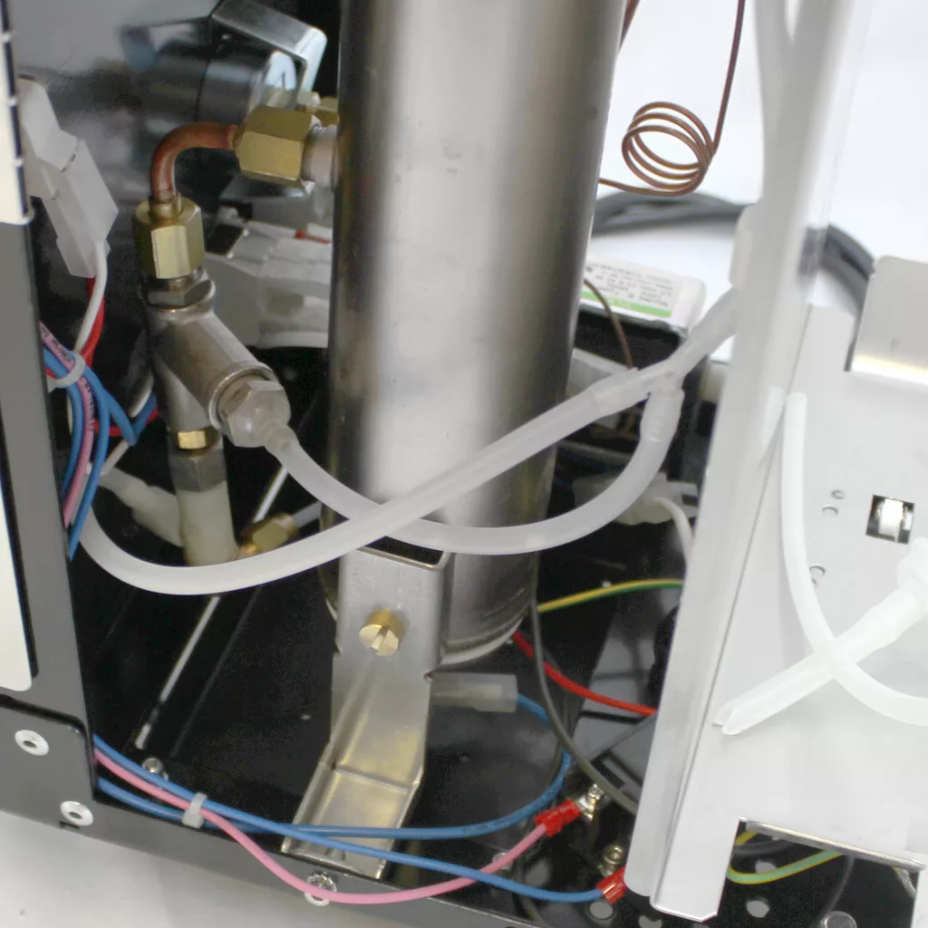 Close-up of the internal components of the Bezzera Unica Espresso Machine, featuring metal pipes, wires, and tubes attached to a vertical cylinder inside this high-quality coffee maker. © 2025 1st-line.com