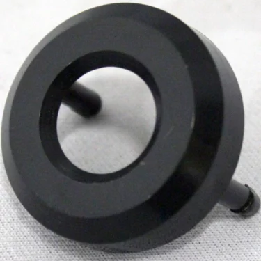 A black, circular plastic Saeco Water seal cap - Royal with a central hole and two short pegs on the back is shown resting on a light gray textured surface. © 2025 1st-line.com