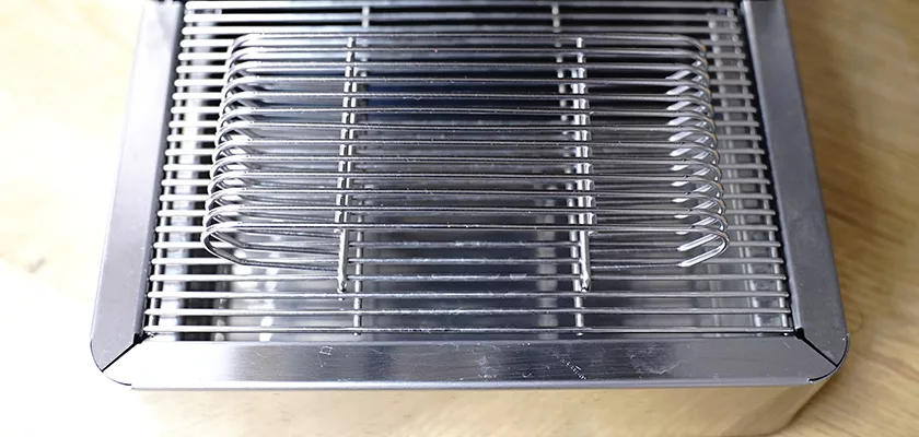 A close-up of a shiny stainless steel wire rack sits atop a rectangular metal container, part of the DISCONTINUED Lelit Victoria PL91T PID Single Boiler Espresso Machine, displayed on a light wooden surface. © 2025 1st-line.com