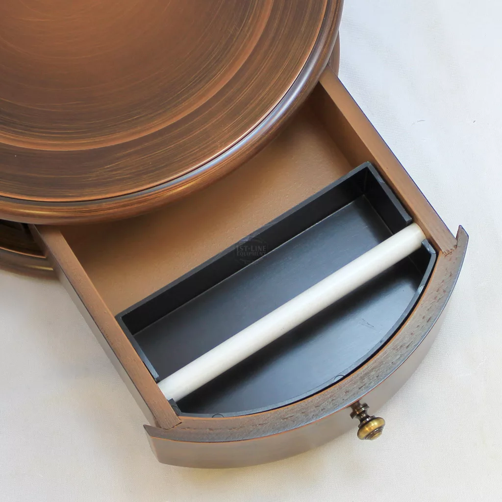 A close-up of an open drawer in the Elektra SB Microcasa Brown Wood Base - 1 drawer, revealing a black tray with a white cylindrical rod inside. The drawer features a small brass knob and sits on a light-colored surface. © 2025 1st-line.com