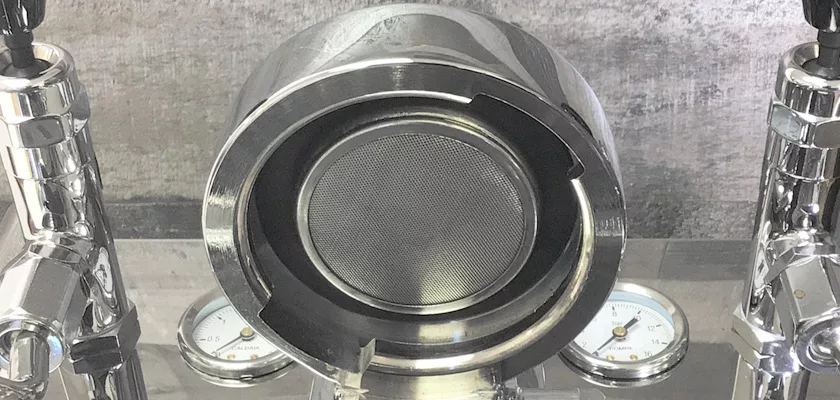 A close-up of the DISCONTINUED ECM Elektronika II Profi HX Espresso Machine’s portafilter holder with a mesh screen, alongside two pressure gauges and metallic components in the background. © 2025 1st-line.com