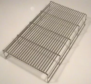 A metal cooling rack with parallel wires and four raised legs, similar to the Fiorenzato A1800176 Grid for Drip Tray for Bricoletta/Volante Tank/Reservoir Model Only, is typically used for cooling baked goods. © 2025 1st-line.com