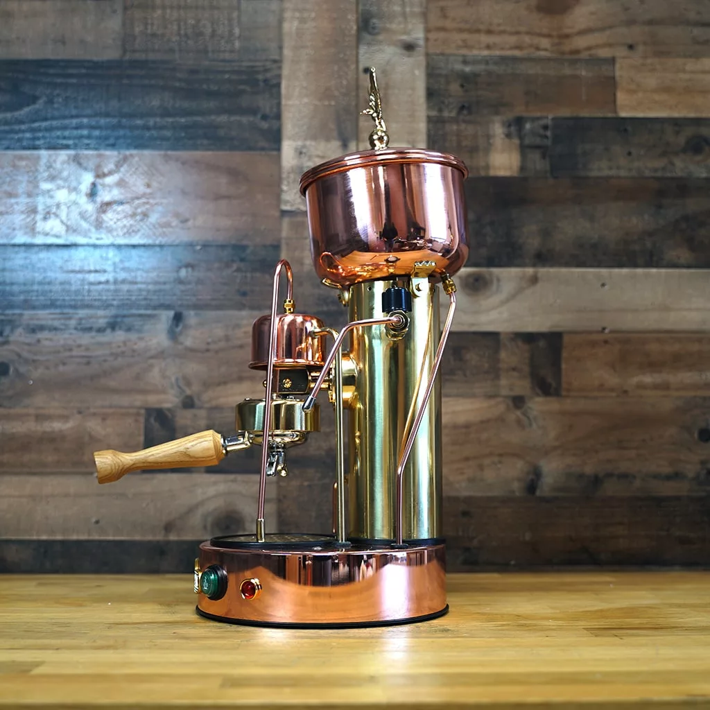 A RETURNED & REFURBISHED Elektra SX Copper & Brass Microcasa Semiautomatica Espresso Machine (C104) with vintage style and wooden handle sits on a wooden counter against a rustic wood-paneled wall. © 2025 1st-line.com