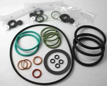 A set of assorted O-rings, gaskets, and sealing washers—including the Elektra 03083034 Gasket Kit for Extramaxi 2 GR 97—arranged on a white surface with extra components in small plastic bags in the background. © 2025 1st-line.com