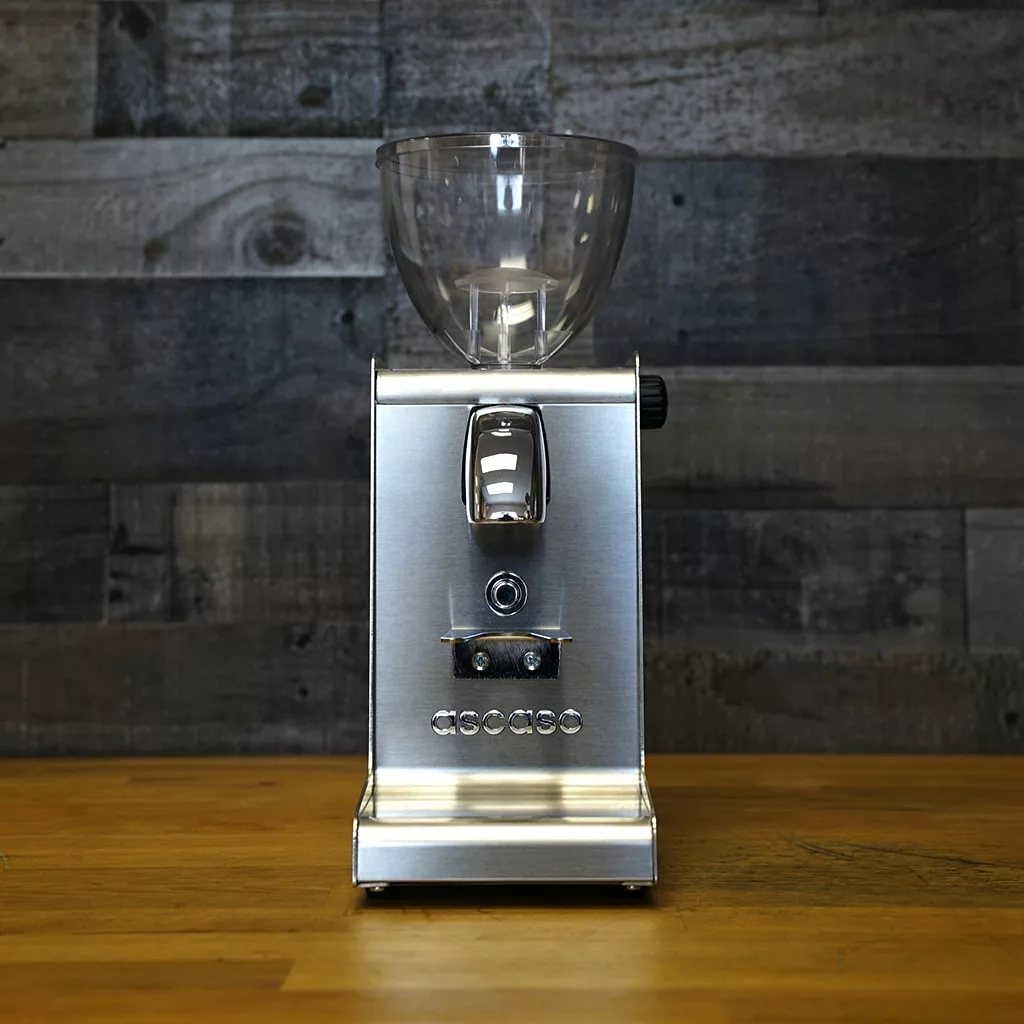 A *SOLD!* SIDEWALK SALE Ascaso I-Steel Conical Burr Espresso Grinder 2018 Model OPEN BOX DISPLAY with central switch and round buttons rests on a wooden counter, highlighting its modern metallic look against a rustic wood wall. © 2025 1st-line.com