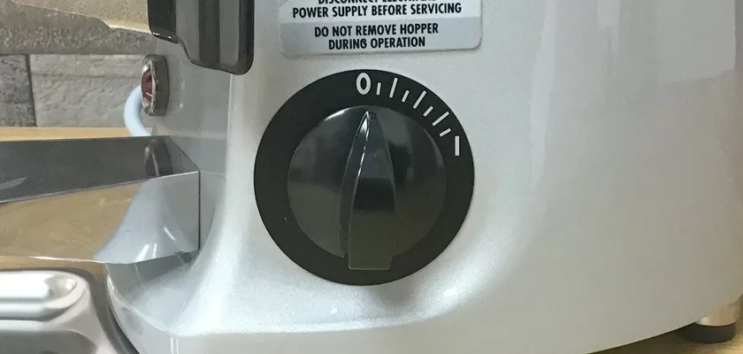 Close-up of a black dial with numbers on the DISCONTINUED Mazzer Mini Timer Doser Espresso Coffee Grinder, showing a label warning to disconnect power and not remove the hopper during operation. © 2025 1st-line.com