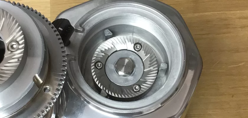 Close-up of a burr set from the DISCONTINUED Quamar M80E V2 On Demand Espresso Coffee Grinder, showing sharp grinding teeth and screws, with part of the metallic housing visible on a light wooden surface. © 2025 1st-line.com