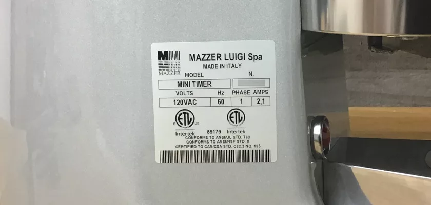 Close-up of a label on the DISCONTINUED Mazzer Mini Timer Doser Espresso Coffee Grinder, showing 120V AC, 60Hz, single phase, 2.1A. Certification logos and Made in Italy are also visible. © 2025 1st-line.com