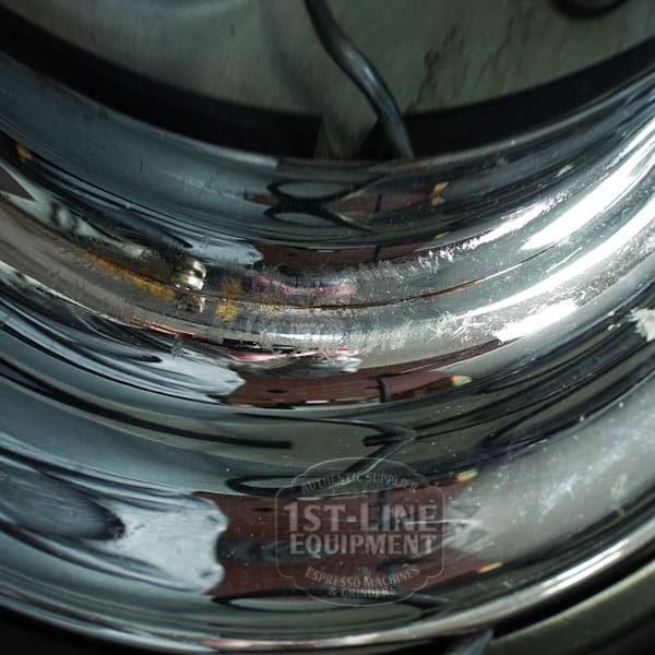 Close-up of a shiny, scratched chrome surface on the SIDEWALK SALE - Elektra Mini Verticale A1C Espresso Machine (E211), reflecting nearby objects in its polished finish. The 1st-Line Equipment logo is faintly visible. © 2025 1st-line.com