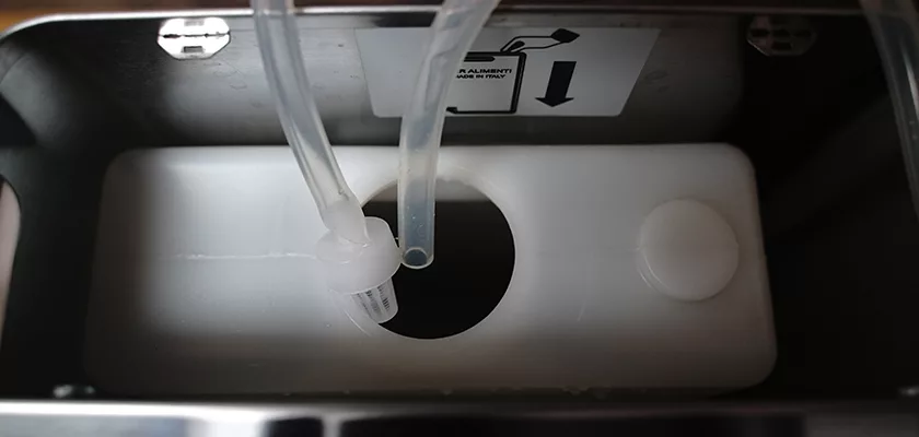 Close-up of an open container with two clear tubes in a round opening on a DISCONTINUED Lelit Victoria PL91T PID Single Boiler Espresso Machine tank; a label with an arrow and instructions is visible above the opening. © 2025 1st-line.com