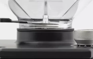 Close-up of the top of a coffee grinder with a clear hopper. Red text on white reads: Eureka Atom Grinder BLOW UP Package. © 2025 1st-line.com