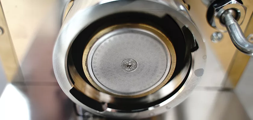 Close-up of the underside of a portafilter on the DISCONTINUED Lelit Victoria PL91T PID Single Boiler Espresso Machine, showing the circular metal filter, group head, and part of the metallic surface. © 2025 1st-line.com