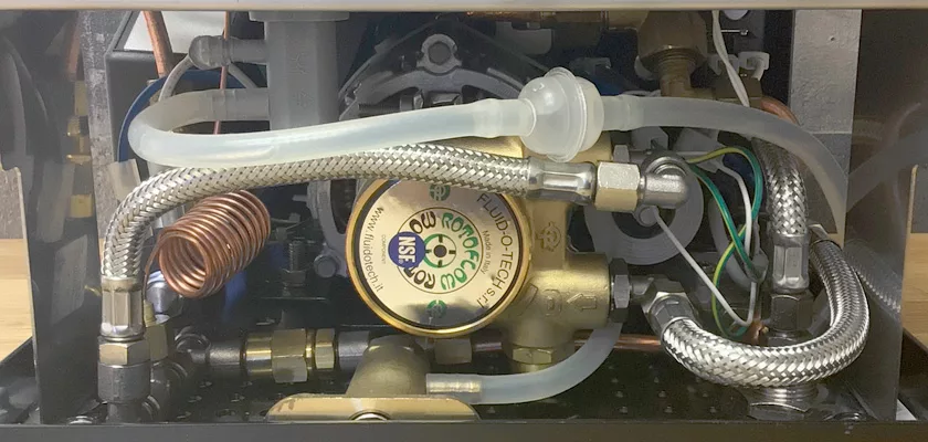 Close-up view of the internal components of the DISCONTINUED ECM Elektronika II Profi HX Espresso Machine, featuring metal pipes, braided hoses, wires, and a brass Fluid-O-Tech pump—key elements of its high-performance system. © 2025 1st-line.com