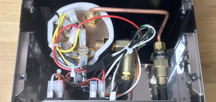 Inside view of the Rancilio Silvia M Espresso Machine showing neatly arranged wires, brass parts, a copper pipe, connectors, and part of the boiler assembly, all secured with zip ties. © 2025 1st-line.com