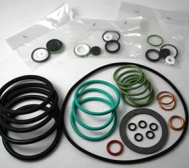 O-rings and gaskets from the Elektra 03084034 Gasket Kit for Barlume 3 GR 97 in black, green, red, and white are arranged on a surface, with additional sets sealed in transparent plastic bags visible in the background. © 2025 1st-line.com