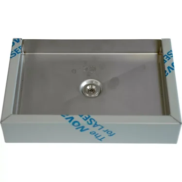 The Bezzera 5340510 Drip Tray is a rectangular stainless steel tray with a central drain, viewed from above. Blue protective film can be seen on the edges of the tray’s frame. © 2025 1st-line.com