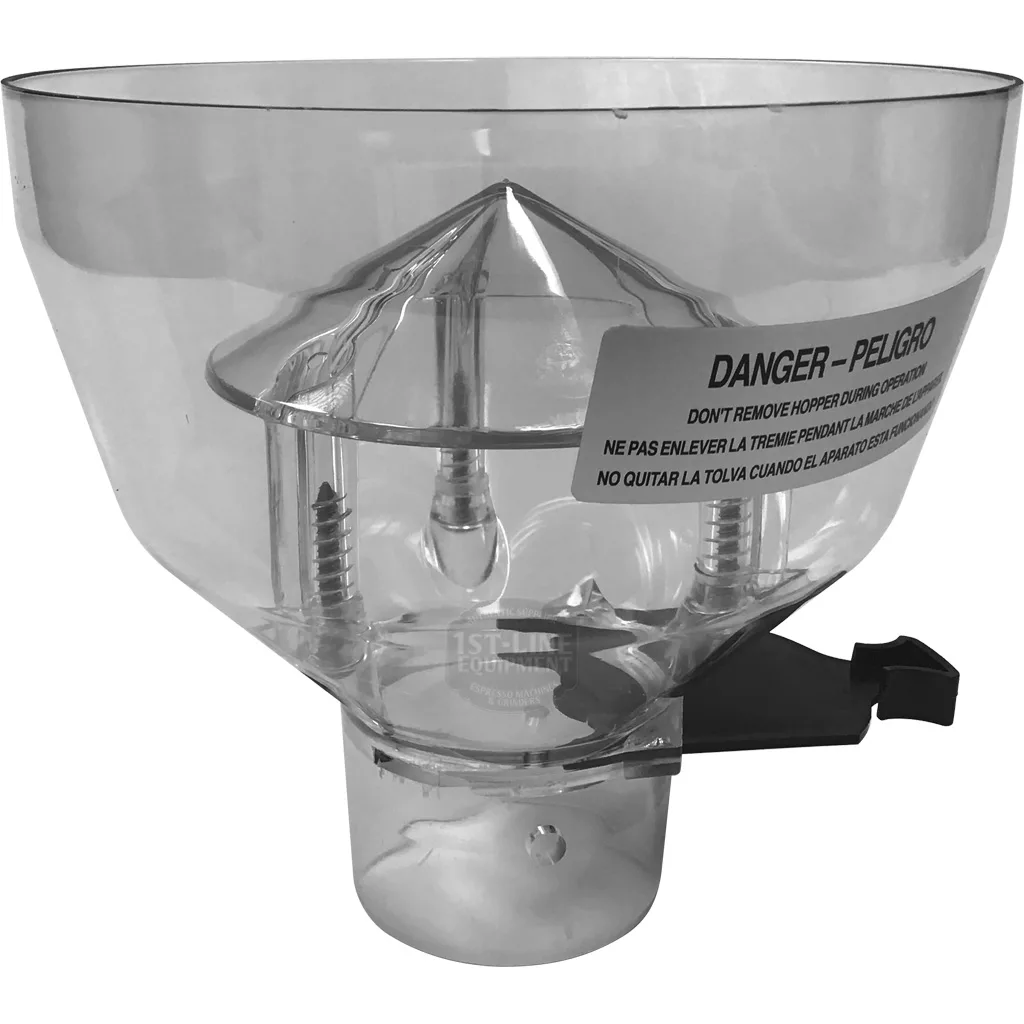 The DISCONTINUED Mazzer SMI0CAE02 Short Bean Hopper features a clear body with visible metal springs and inner parts, an English/Spanish warning label, and a black Mazzer lever on the side. © 2025 1st-line.com