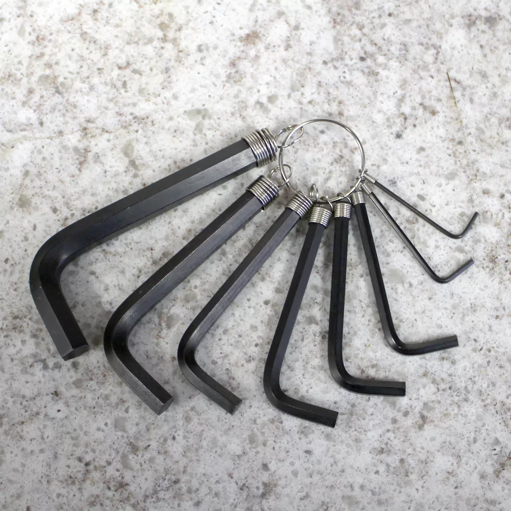 The Hex Key Set - 8 piece includes black Allen wrenches in assorted sizes, attached to a metal key ring and displayed on a light speckled surface. © 2025 1st-line.com