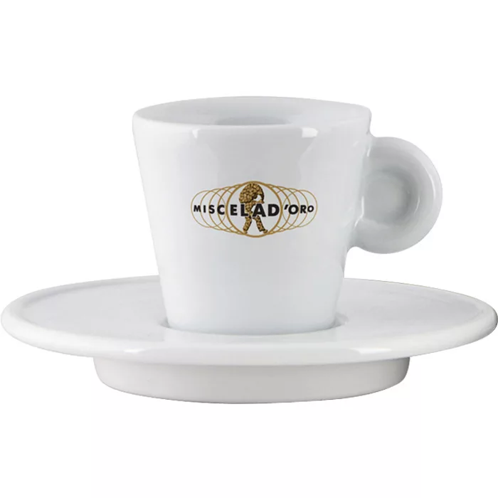 The Miscela dOro Espresso Cup & Saucer - 2 fl oz is a white porcelain cup with a handle, displaying the gold and black Miscela dOro logo on the front, paired with a matching saucer. © 2025 1st-line.com
