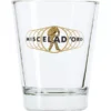 The Miscela dOro Espresso Shot Glass - 3 fl oz is a clear glass featuring the gold Miscela dOro logo, text, and a walking figure surrounded by overlapping gold circles. © 2025 1st-line.com