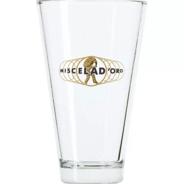 The Miscela dOro Latte Glass is a clear coffee glass with a gold Miscela dOro logo and an illustration of a walking figure carrying a large sack. © 2025 1st-line.com