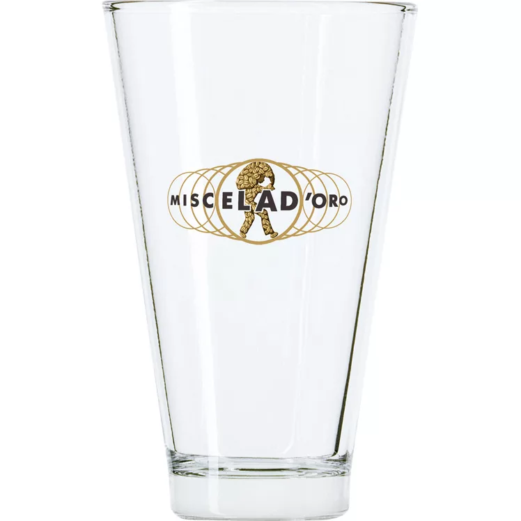 The Miscela dOro Latte Glass is a clear coffee glass with a gold Miscela dOro logo and an illustration of a walking figure carrying a large sack. © 2025 1st-line.com