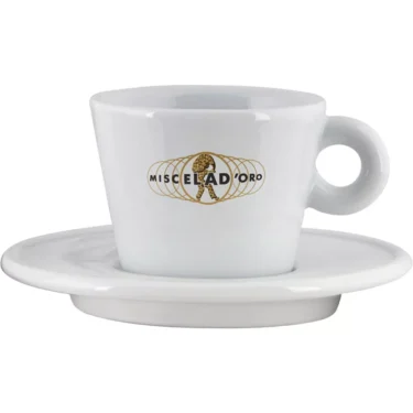 The Miscela dOro Modern Latte Cup & Saucer (9.5 fl oz) is a white ceramic cup with a handle, featuring a gold logo with the brand name and a coffee bean globe with a walking figure, set on a matching saucer. © 2025 1st-line.com