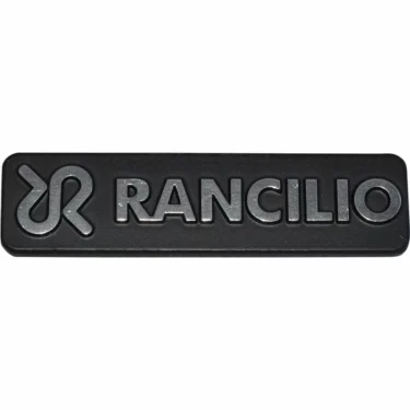 The Rancilio 42200121 Nameplate Logo is a black rectangular badge featuring the Rancilio nameplate and stylized silver emblem embossed on its surface. © 2025 1st-line.com