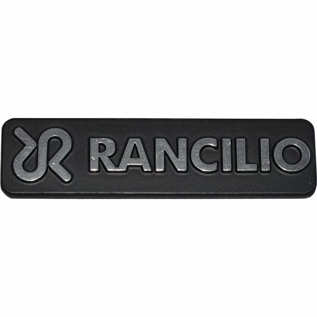 The Rancilio 42200121 Nameplate Logo is a black rectangular badge featuring the Rancilio nameplate and stylized silver emblem embossed on its surface. © 2025 1st-line.com