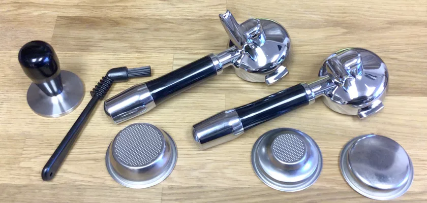 Two portafilters, three filter baskets, a tamper, and a cleaning brush are displayed on wood—ideal accessories for the DISCONTINUED ECM Elektronika II Profi HX Espresso Machine. © 2025 1st-line.com