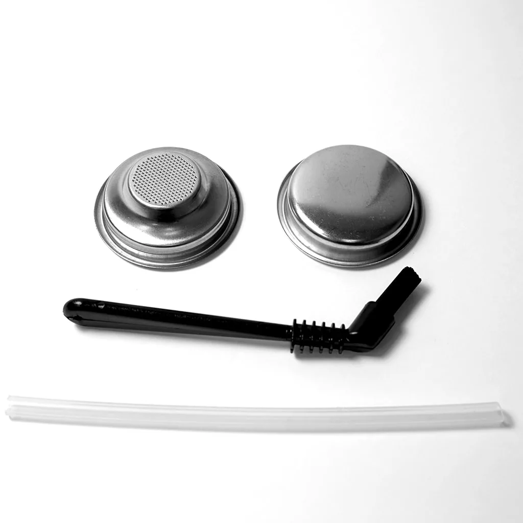Two round metal filters, a black cleaning brush, and a white straw—accessories for your discontinued ECM Classika PID Espresso Machine—are arranged on a white background to look like a smiling face. © 2025 1st-line.com