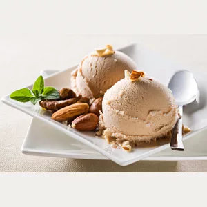 Two scoops of ice cream made with DISCONTINUED Antico Eremo Hazelnut Gelato & Sorbet Powder Mix - 2.2lb bag, served on a white square plate and garnished with assorted nuts, a mint sprig, and a spoon. © 2025 1st-line.com