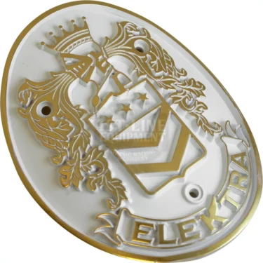 The Elektra 02858062 Emblem - Belle Epoque is a gold and white oval emblem with a crowned knight’s helmet, shield with stars and stripes, ornate foliage, “Elektra” at the bottom, and three mounting holes. © 2025 1st-line.com