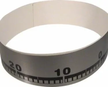 The Rancilio 45010044 Bean Hopper Sticker for Rancilio Rocky is a gray circular sticker with black measuring-tape style markings, including visible numbers 10 and 20, designed to form a loop on the bean hopper. © 2025 1st-line.com