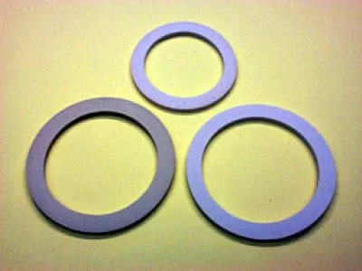Three Brasil 10-3 Cup Moka Pot Gasket Replacements, two large and one small, are arranged in a triangle on a pale yellow surface—perfect for replacing worn gaskets in your Moka pot. © 2025 1st-line.com