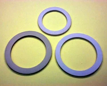 Three flat, circular Brasil 10-9 Cup Moka Pot Gasket Replacements are arranged on a light yellow surface, with two larger gaskets below and a smaller one above them. © 2025 1st-line.com