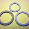 Three flat, circular washers—resembling Brasil 10-6 Cup Moka Pot Gasket Replacement rings—are arranged on a light yellow surface, with a smaller washer placed above two larger ones. © 2025 1st-line.com
