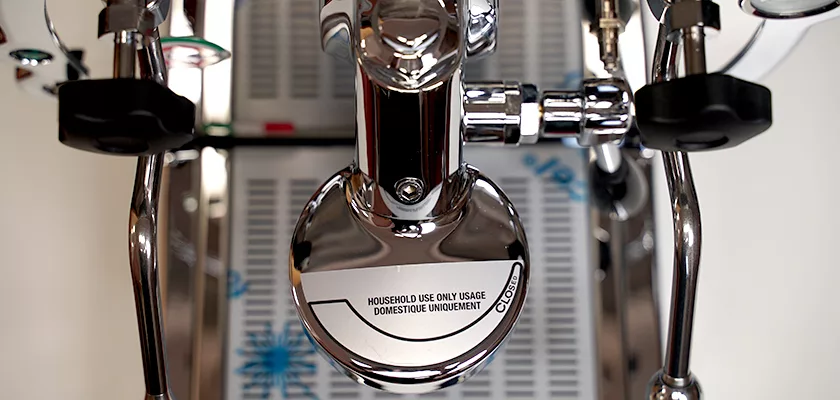 Close-up of the DISCONTINUED La Nuova Era Cuadra HX Espresso Machine with a chrome finish. HOUSEHOLD USE ONLY is visible on a circular part, reflecting light and nearby details. © 2025 1st-line.com